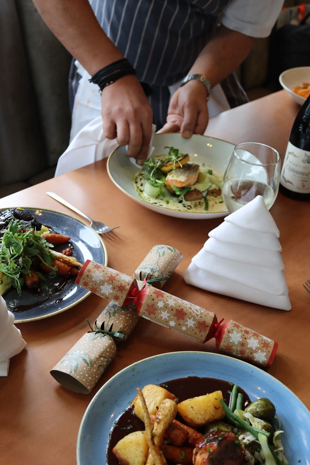 An overhead view of a festive table with plated courses, crackers, folded napkins and glasses ready for guests