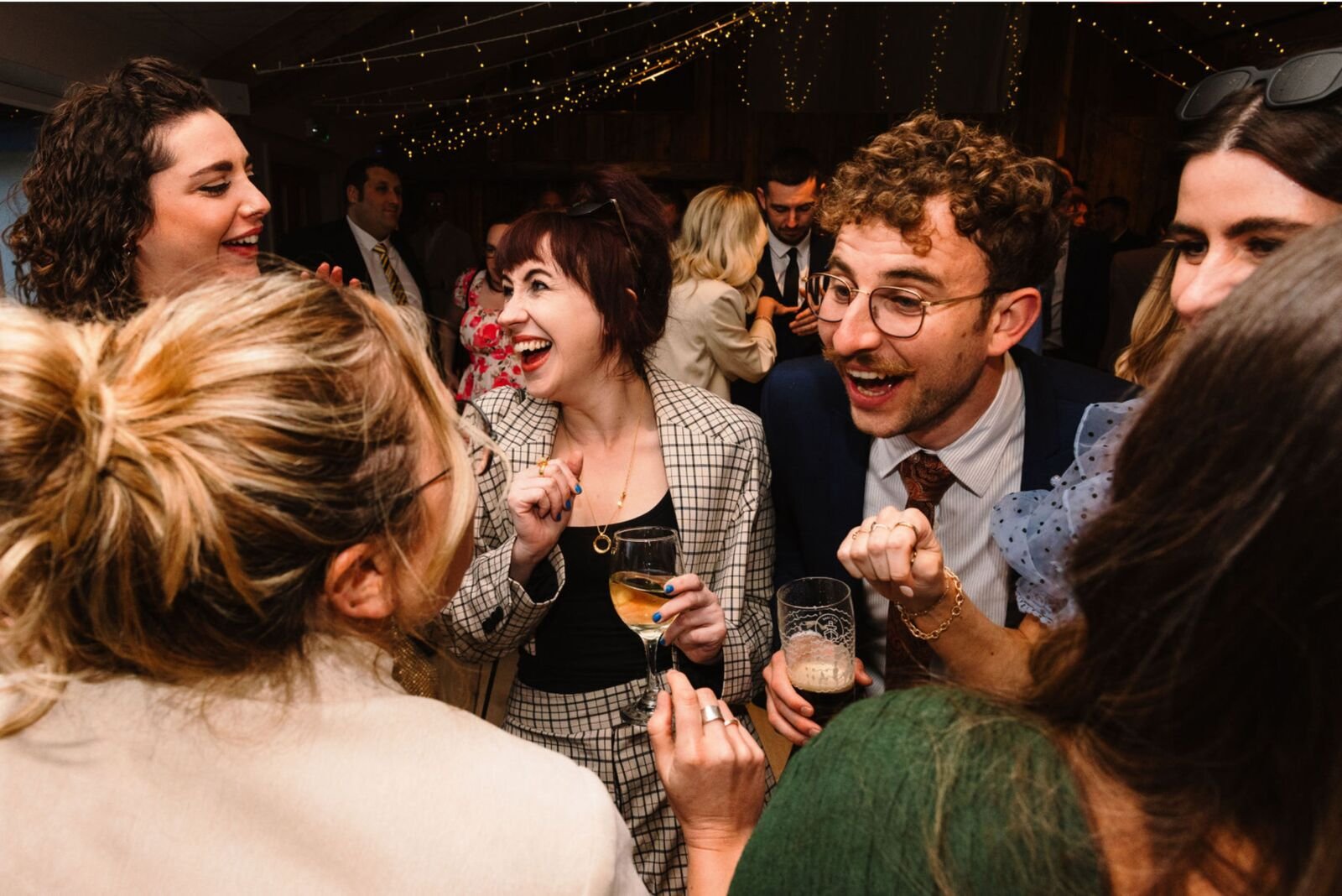 Guests laughing together with drinks in hand under strings of fairy lights