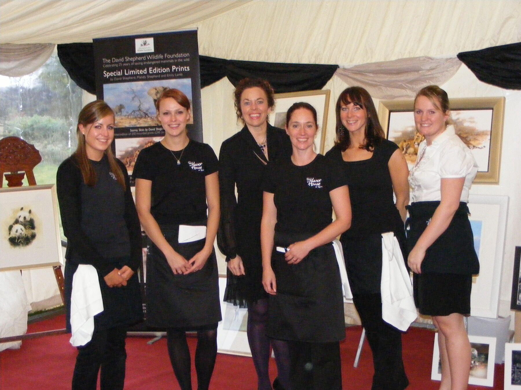 Six members of the front of house team standing together in Manor House branded shirts and aprons, service cloths over their arms