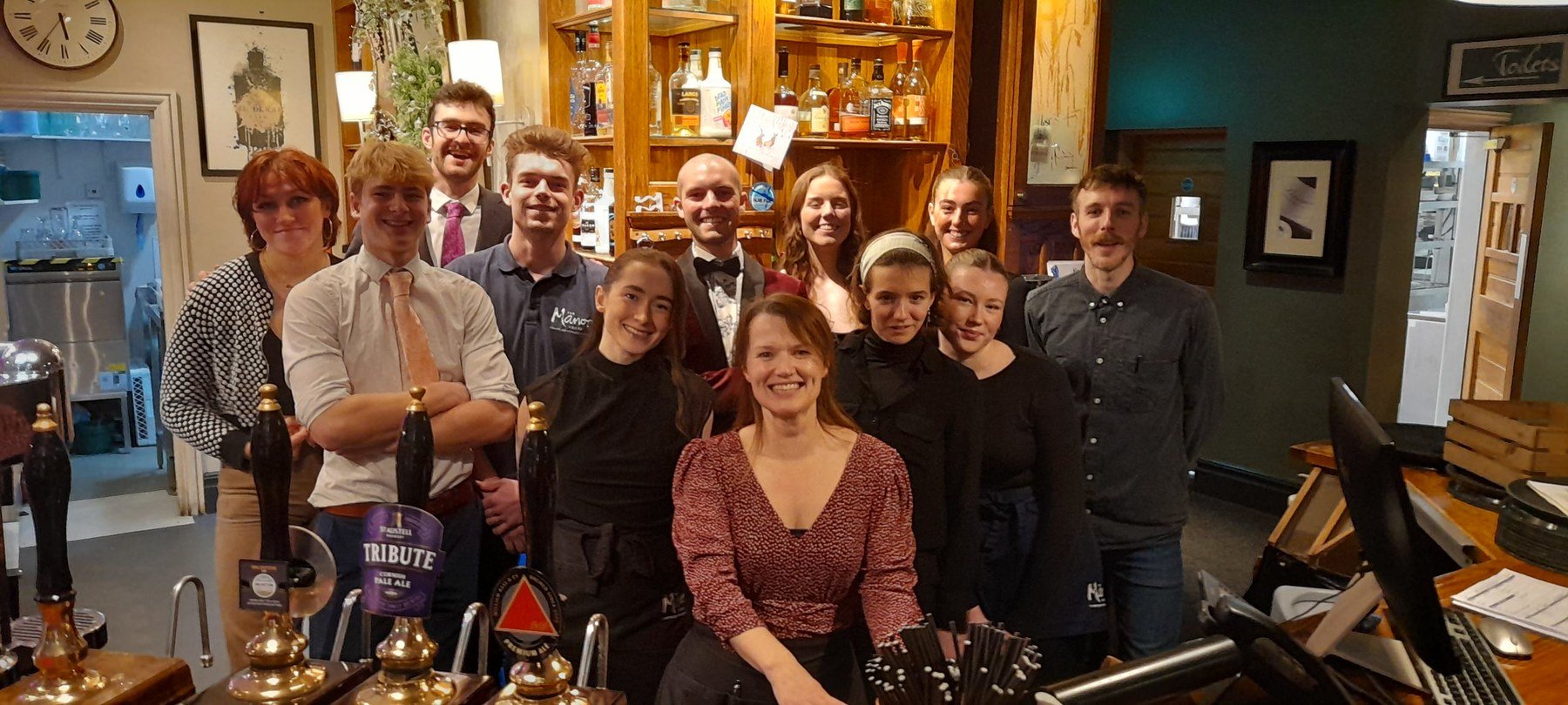 The whole team gathered together behind the bar for a photograph, a dozen of them, in front of the optics and the hand pumps