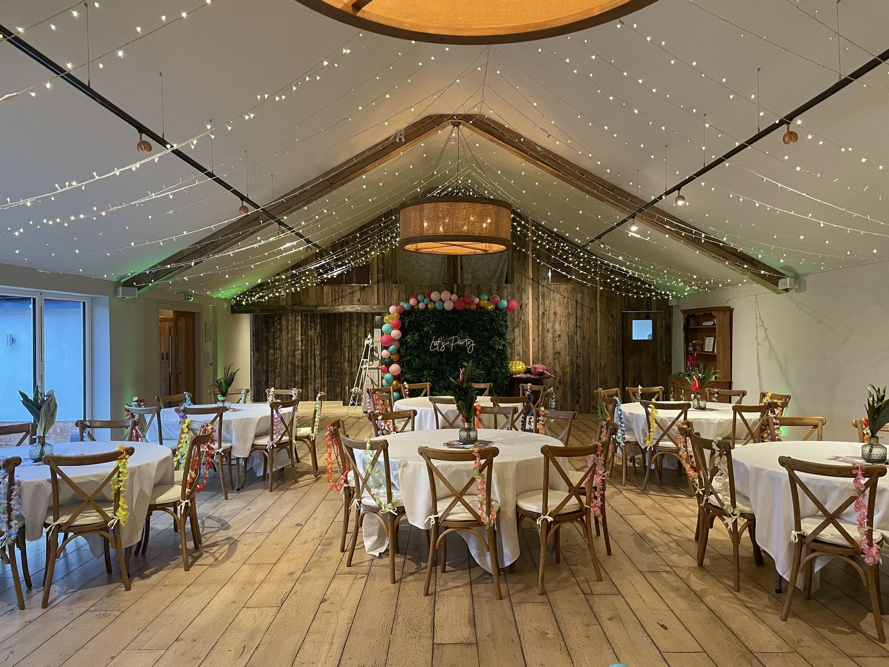 The Pavilion dressed for a party with a balloon arch, a foliage wall and a neon sign reading Let's Party, tables laid with white linen