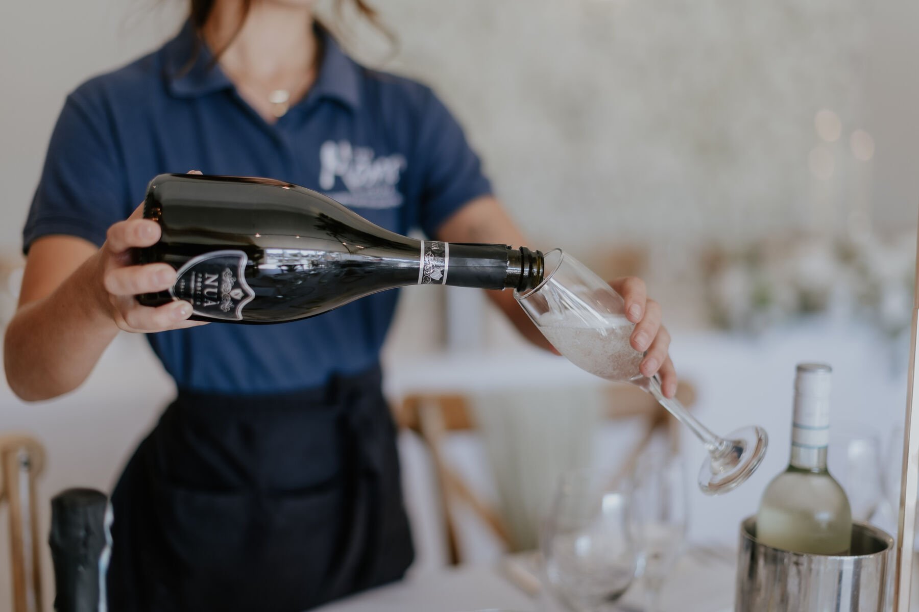 A member of the team pouring prosecco into a flute at a dressed table, bottles chilling in an ice bucket behind