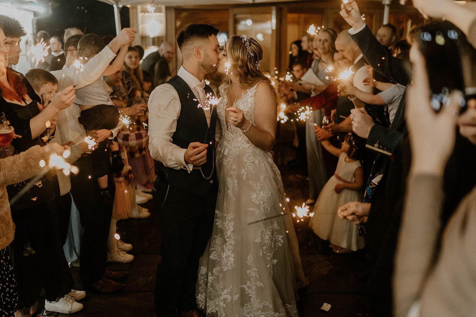 A couple kissing beneath an archway of sparklers held up by their guests at the end of the night